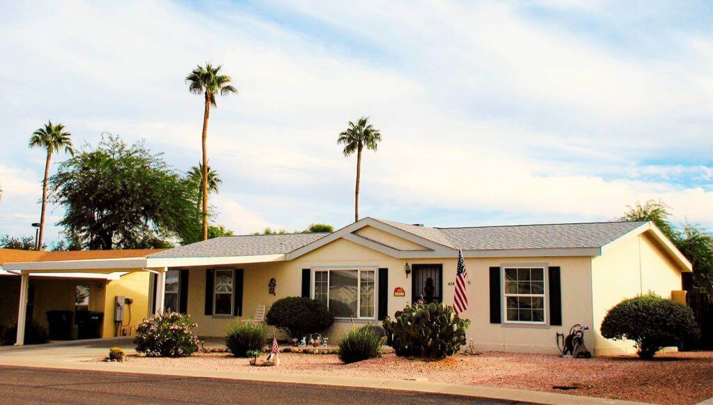 Exterior of a single story manufactured home with a side garage, front lawn and palm trees in the background
