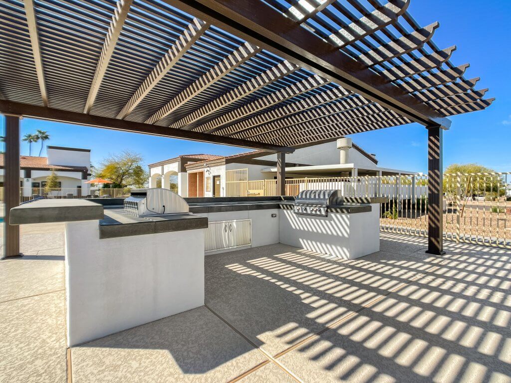 Two steel grills built-in a marble and concrete structure under the shade of a wooden pergola